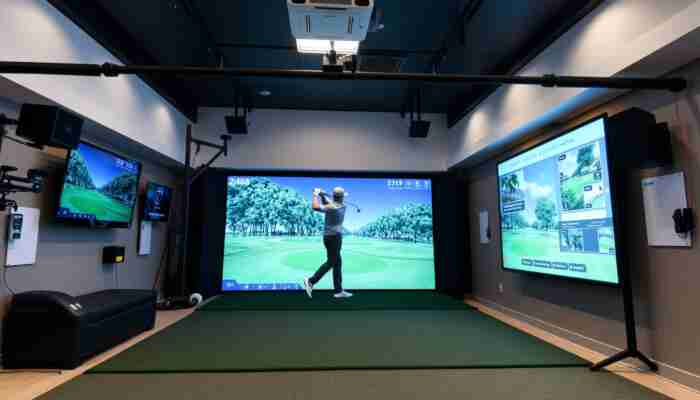 High-tech indoor golf simulator setup showcasing seamless hardware integration with projectors, sensors, and screens, featuring high-speed cameras and advanced tracking systems in a modern space, while a golfer practices their swing using a user-friendly touchscreen interface surrounded by virtual golf course graphics.