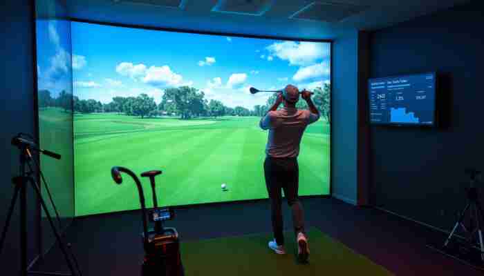 Golfer practicing in an indoor golf simulator while reviewing ball and club data